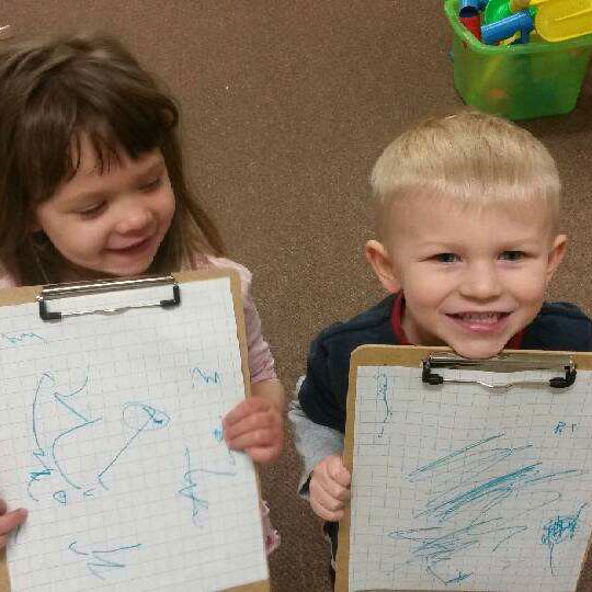 Two children who attend Kinder Haus hold up their newest artwork. 