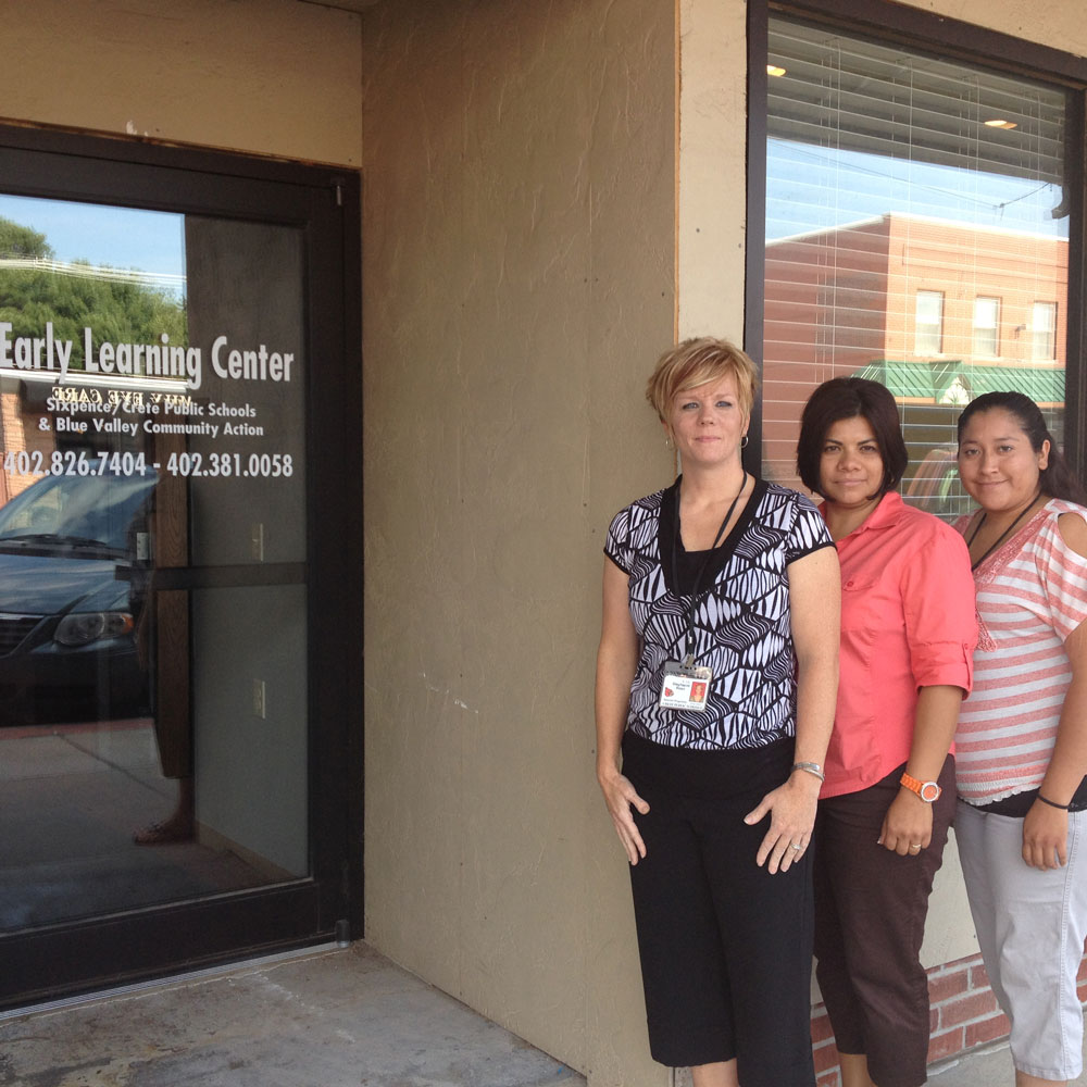 Stephanni (l), Lorena (m) are standing outside of Lorena's workplace: Sixpence Crete Public Schools & Blue Valley Community Action.
