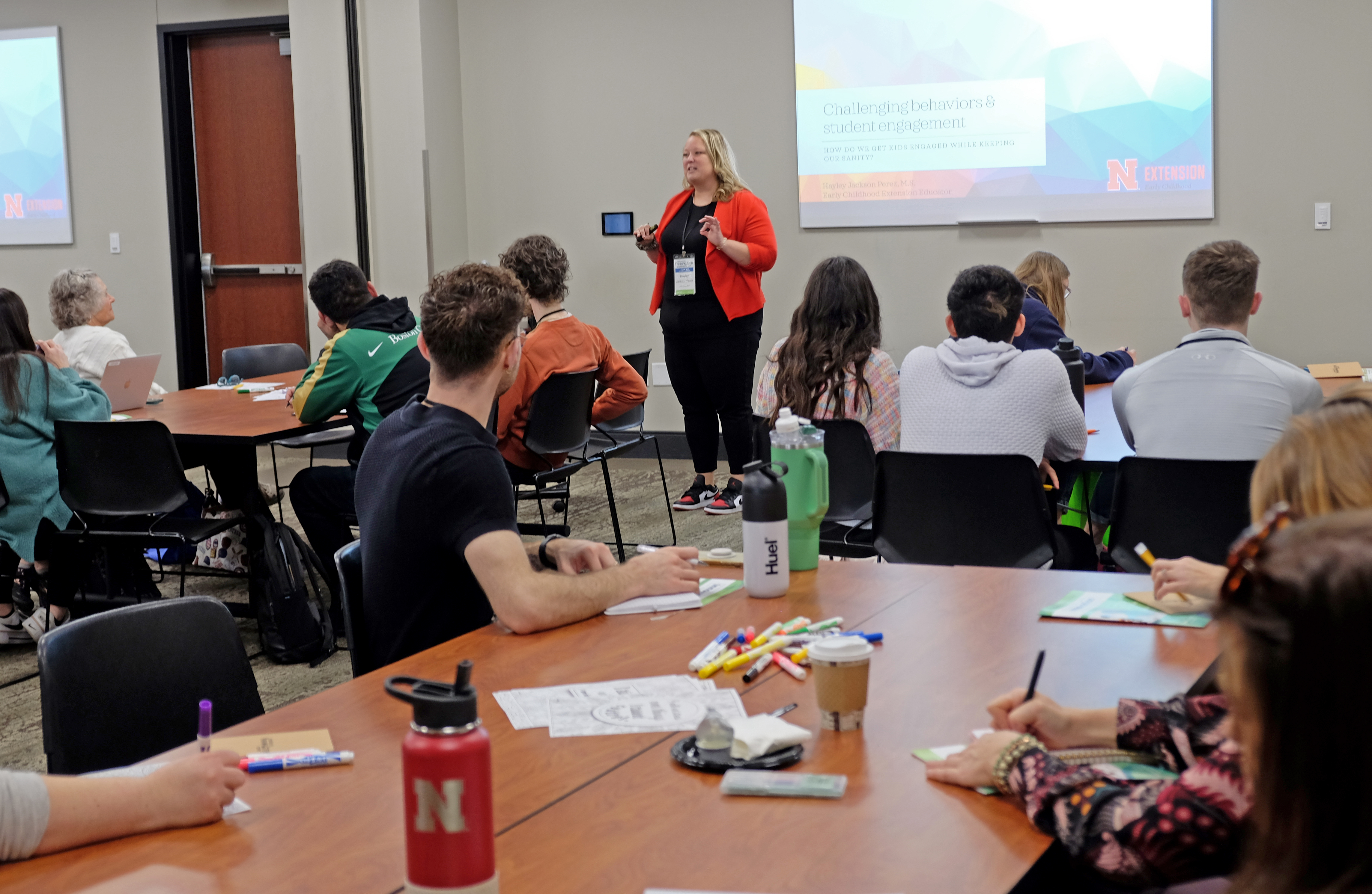 The presenter stands in front of a full room.